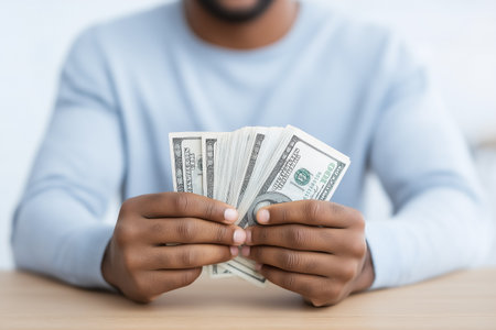 Individual organizes crisp cash notes with focus in a neutral-toned space. Clean wooden surface enhances financial awareness. Concept of financial services, budgeting, personal finance.の素材