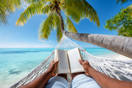 Individual laying in hammock reading book while enjoying stunning ocean view. Bright sunny day with clear blue sky and tranquil water. Concept of relaxation, vacation, leisure.の素材