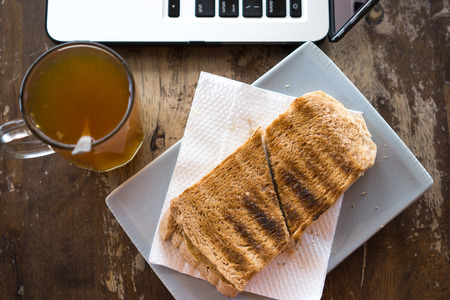 Hot tea, bread and laptop on wooden table.の写真素材