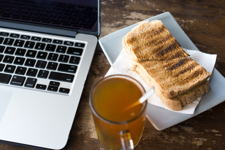 Hot tea, bread and laptop on wooden table.の写真素材