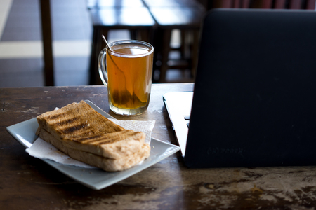 Hot tea, bread and laptop on wooden table.の写真素材