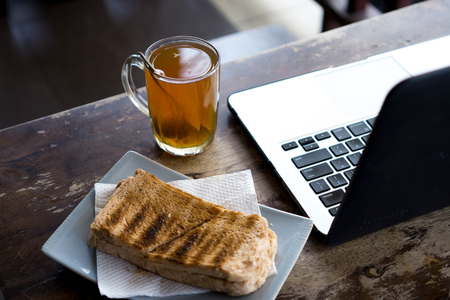Hot tea, bread and laptop on wooden table.の写真素材