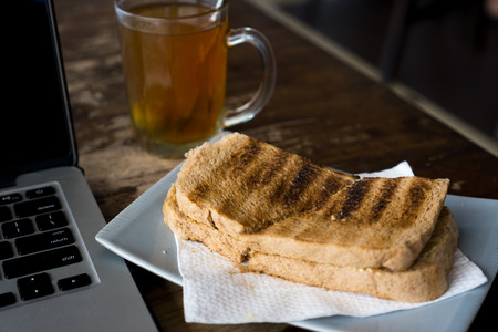 Hot tea, bread and laptop on wooden table.の写真素材