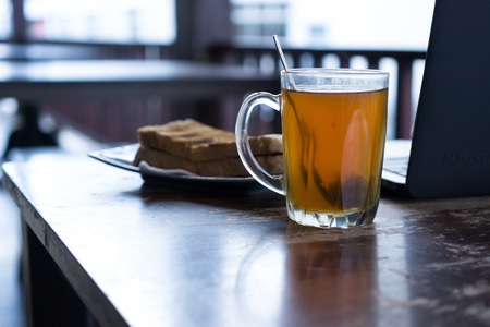 Hot tea, bread and laptop on wooden table.の写真素材