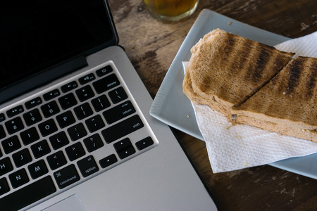 Hot tea, bread and laptop on wooden table.の写真素材