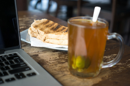 Bread, hot tea and laptop on wooden table.の写真素材