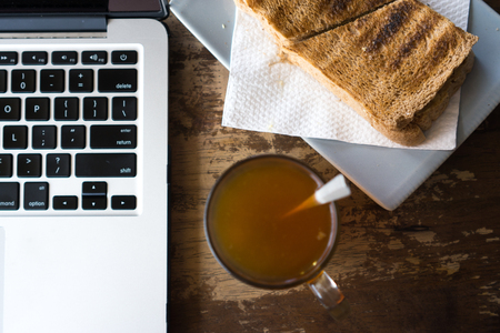 Bread, hot tea and laptop on wooden table.の写真素材