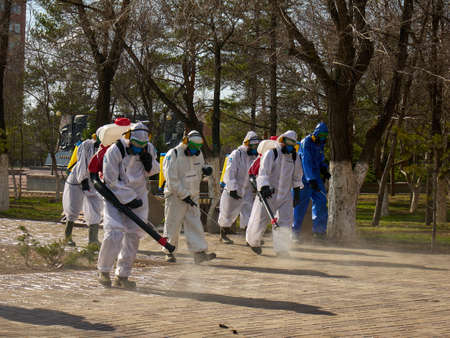 A men in a protective disinfection suits sprays sterilizer on the park square and sidewalk to prevent spread of coronavirus covid-19のeditorial素材