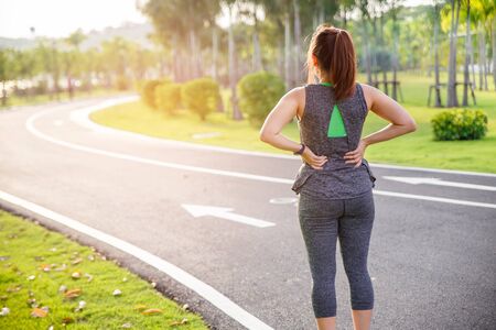 Female runner athlete back injury and pain. Woman suffering from painful lumbago while running in...