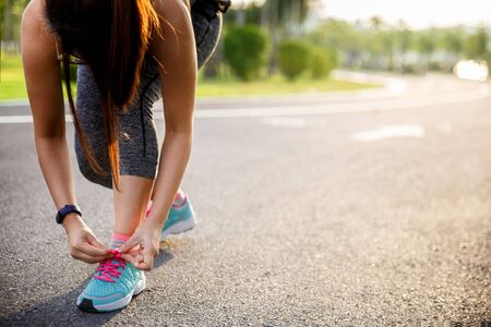 Woman runner tying running shoes before run for exercise in the morning. Woman runner checking shoe in order to get ready to run.の写真素材