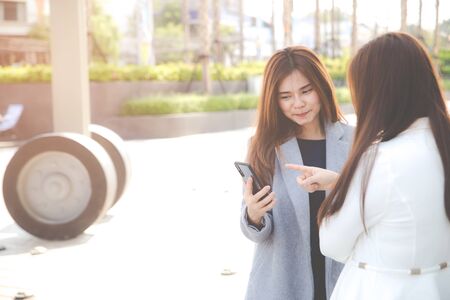 Two confident businesswomen standing together outside and show something on smart phone. Business concepts.の写真素材