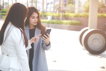 Two confident businesswomen standing together outside and show something on smart phone. Business concepts.の写真素材