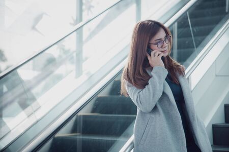 Beautiful confident businesswoman talking something on smart phone and walking inside in airport. Casual young businesswoman wearing blue dress with gray suit.の写真素材