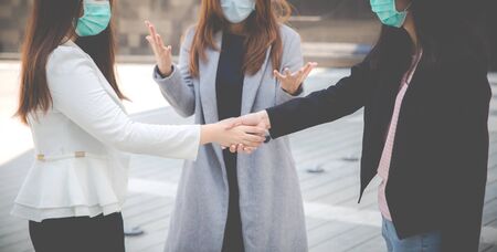 Businesswomen shaking hands with people in the background. Two confident businesswomen shaking hands and wearing face protection in prevention for coronavirus. Business concepts, Air pollution, Coronavirus pandemic, environmental concept.の写真素材