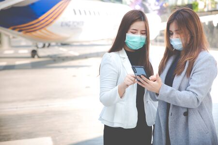 Two confident businesswomen standing together outside, show something on smart phone and wearing face protection in prevention for coronavirus. Business concepts, Air pollution, Coronavirus pandemic, environmental concept.の写真素材