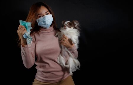Woman wearing face mask and hoding a dog on dark background, gesture up confidence to fight the crisis, anti smog and protect her from virus. Coronavirus pandemic.の写真素材