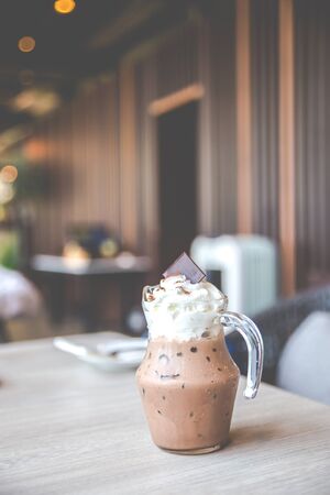 Iced cocoa drink with whipping cream topping on the wooden table in cafe.の写真素材