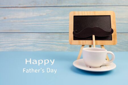Happy Father's day concept. A black mustache paper, a cup of coffee, blackboard and the text written that Happy Father's Day on blue background.の写真素材