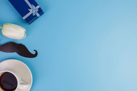 Happy Father's day concept. A black mustache paper, a cup of coffee and blue box isolated on blue background.の写真素材