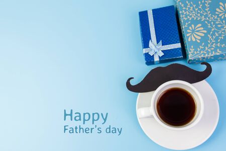 Happy Father's day concept. A black mustache paper, a cup of coffee, blue box and the text written that Happy Father's Day on blue background.の写真素材