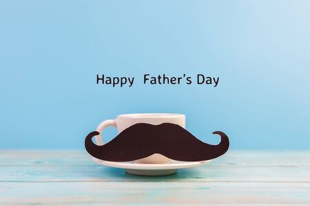 Happy Father's day concept. A black mustache paper, a cup of coffee and the text written that Happy Father's Day on blue background.の写真素材