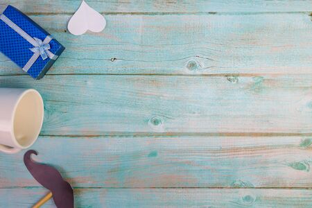 Happy Father's day concept. A black mustache paper, a cup of coffee, blue box and and a white heart paper on blue wooden.の写真素材