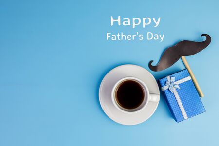 Happy Father's day concept. A black mustache paper, a cup of coffee, blue box and the text written that Happy Father's Day on blue background.の写真素材