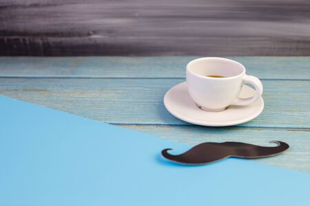 Happy Father's day concept. A black mustache paper and a cup of coffee isolated on blue background.の写真素材