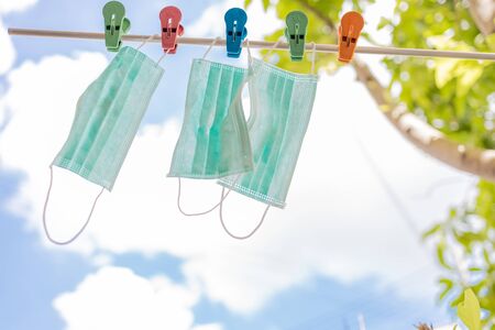 Three surgical face masks drying in sun on a rope with blue sky in background.