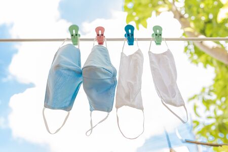 Four surgical face masks drying in sun on a rope with blue sky in background.の写真素材