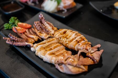 Close up the squid with sweet sauce and sesame seeds on the black plate with blur of the japanese food set. Traditional in Japanese food.の写真素材
