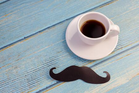 Happy Father's day concept. A black mustache paper, a cup of coffee, blue box isolated on blue wooden.の写真素材