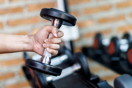 Closeup a man's hand holds a dumbbell with his right hand in the gym, Concept for exercise and health care.の写真素材
