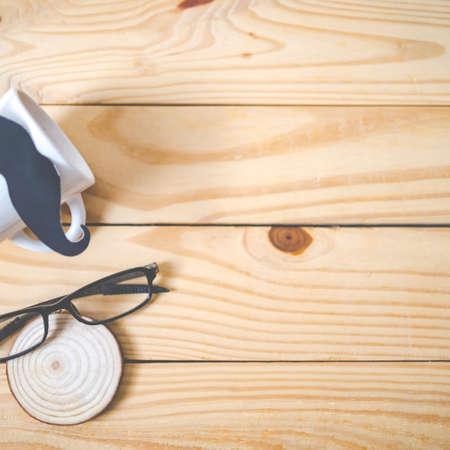 Happy Father's day concept. A black mustache paper, a blue necktie, a blue gift box and glasses on wooden table.の写真素材