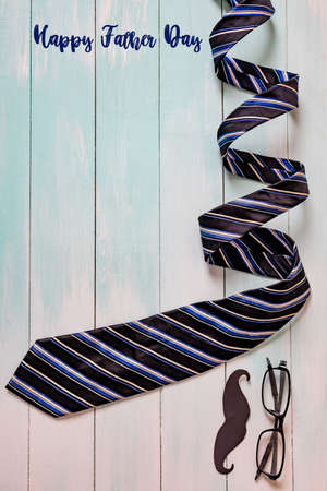 Happy Father's day concept. A black mustache paper, a blue necktie and glasses on wooden table.