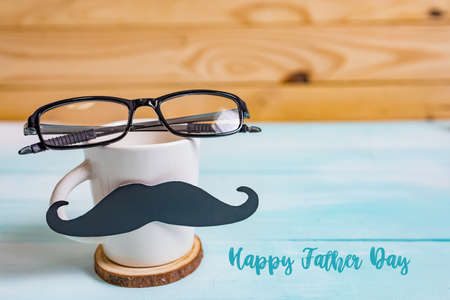 Happy Father's day concept. A black mustache paper, a cup of coffee and glasses on wooden table.の写真素材