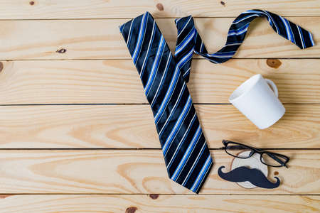 Happy Father's day concept. A black mustache paper, a blue necktie, a blue gift box and glasses on wooden table.の写真素材