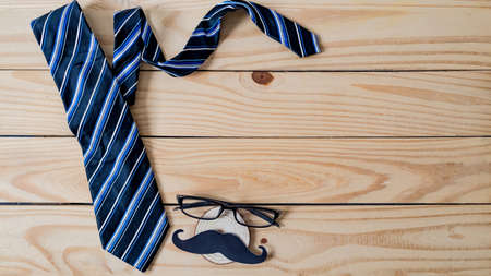 Happy Father's day concept. A black mustache paper, a blue necktie and glasses on wooden table.の写真素材