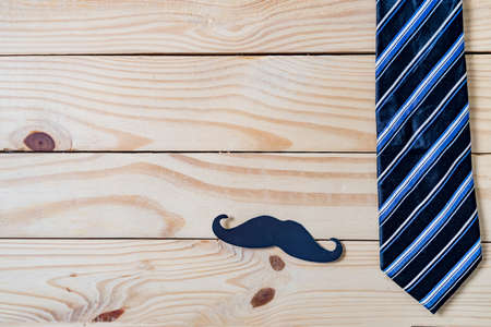 Happy Father's day concept. A black mustache paper, a blue necktie and glasses on wooden table.の写真素材
