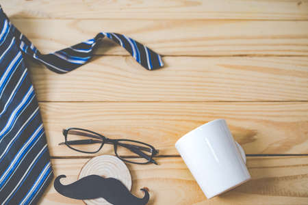 Blur of Background, Happy Father's day concept. A black mustache paper, a blue necktie, a blue gift box and glasses on wooden table.の写真素材