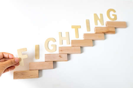 Focus of hand arranging wood block stacking as step stair. Business concept for growth success process. Stairs up as a symbol of career growth up or business success. the word written the FIGHTING.の写真素材