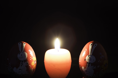 red easter egg shape candle burning between two wooden eggsの写真素材