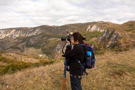 Woman tourist photographer with camera on a mountain outdoors during a hike in autumnの写真素材