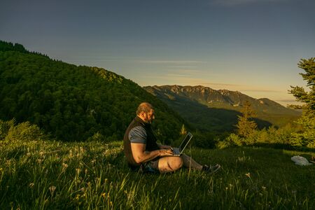man working outdoors with laptop. Green spring mountain landscape
