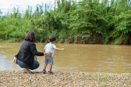 mother watching over her child stands watching the river on the beachの写真素材