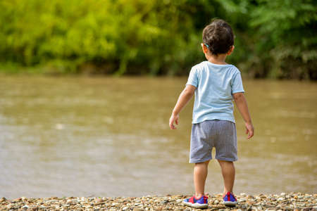 A 2-year-old Asian boy looks suspiciously at the river on the beach.の写真素材