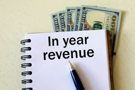 IN YEAR REVENUE words in a notebook with a pen against the background of dollar bills. Business and...