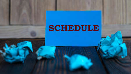 SCHEDULE - words on blue paper on a dark wooden background with crumpled pieces of paper. Business and finance concept.の写真素材