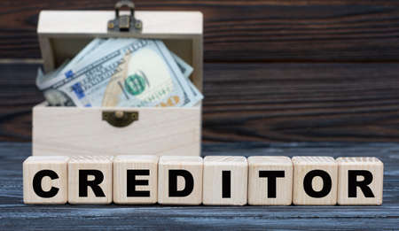 CREDITOR word on cubes with a chest of money against a dark background. Business and finance concept