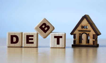 DEBT word on cubes on a light background with a wooden house. Business and finance concept.の写真素材